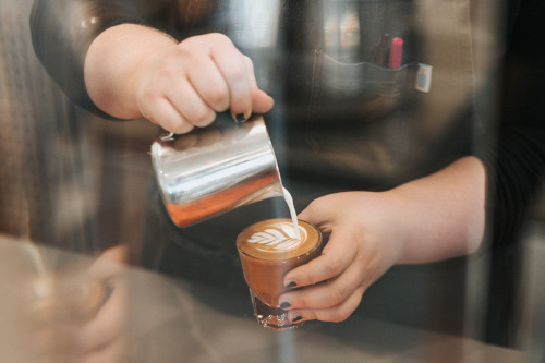 A barista pouring a cortado coffee
