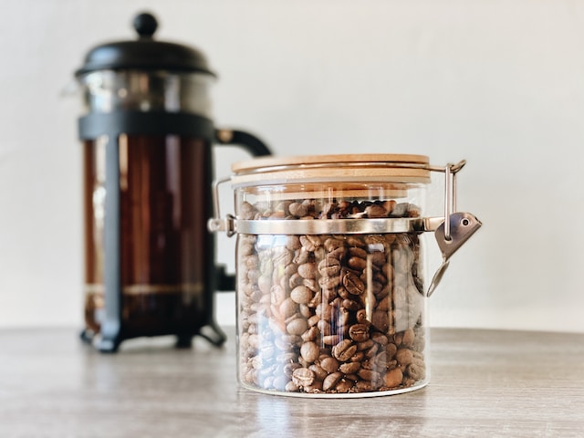 French Press in background with a jar of juicy coffee beans in the front. What beans are the best to try for a French Press coffee at home?